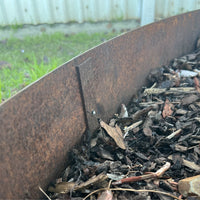 Close-up of a Corten Steel Garden Edging Peg installed in a garden, showing weathered appearance blending with the natural ground.