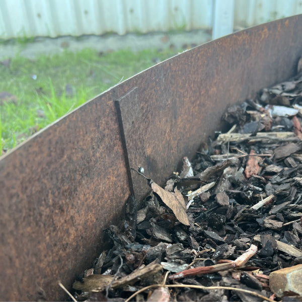 Close-up of a Corten Steel Garden Edging Peg installed in a garden, showing weathered appearance blending with the natural ground.