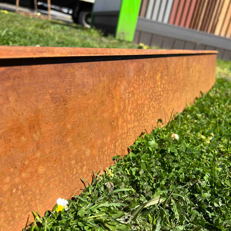 Close-up of Corten Steel Garden Edging with a visible rust-like finish, installed on a grassy area.