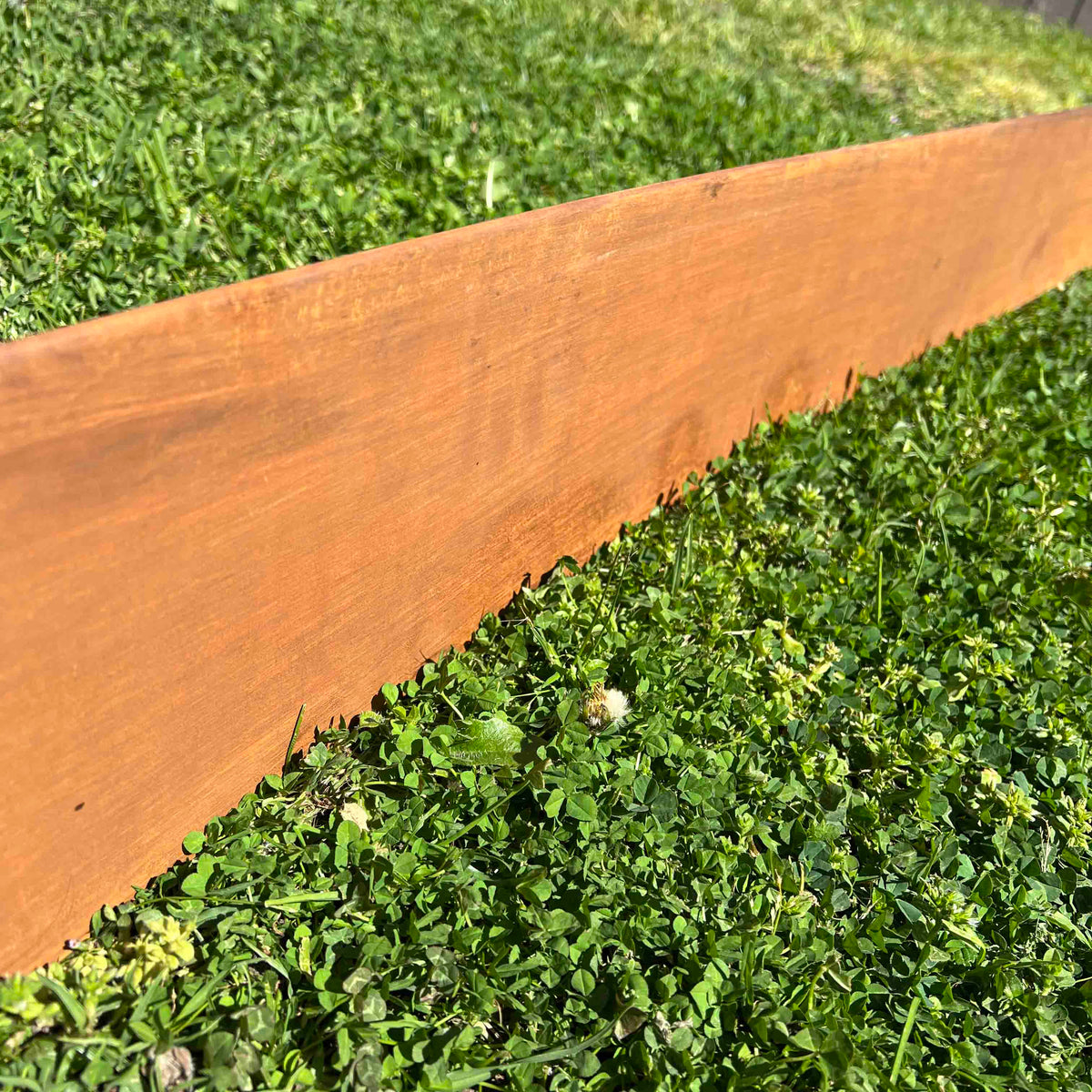 Close up of smooth-look corten steel edging and rusted metal garden edging installed as a lawn divider.