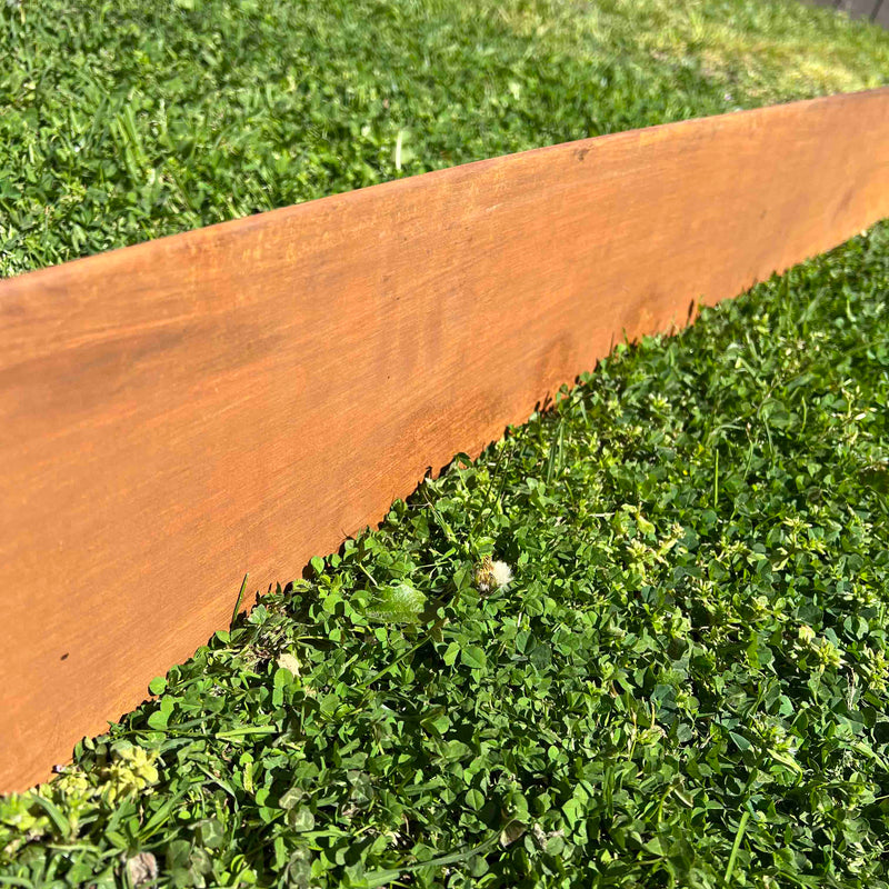 Close up of smooth-look corten steel edging and rusted metal garden edging installed as a lawn divider.